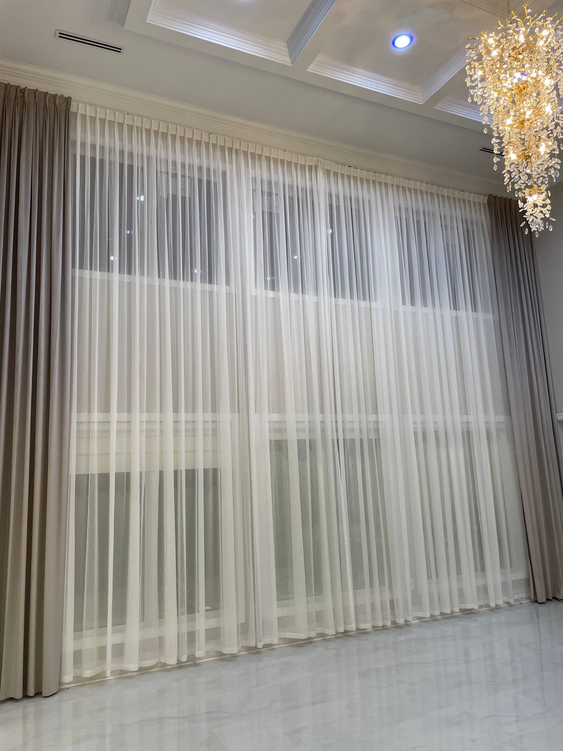 Elegant floor-to-ceiling cream silk drapes with gold tiebacks in luxury living room